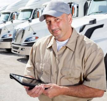 Man in uniform with ipad standing in front of several large trucks